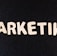 Wooden letters arranged to spell the word 'MARKETING' on a black textured background.