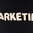 Wooden letters arranged to spell the word 'MARKETING' on a black textured background.